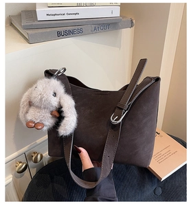 Detail of dark brown tote bag with suede texture and cute white plush rabbit charm