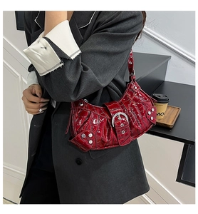 Detail of dark red croc-embossed shoulder bag with silver buckles and punk style rivets