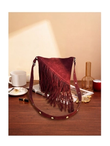 Close-up of burgundy suede fringe shoulder bag on wooden table with retro bohemian style