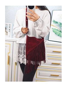 Detail of burgundy suede crossbody bag with long fringes and bohemian vintage tassel style