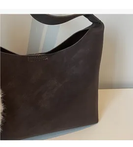 Close-up of vintage brown leather hobo bag with pebble texture and fuzzy ball charm