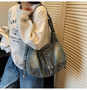Détail d'un sac bandoulière en denim délavé avec des rivets argentés et style punk