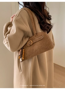 Detail einer braunen Wildleder-Retro-Handtasche mit Metallschnalle und Holzperlen-Anhänger