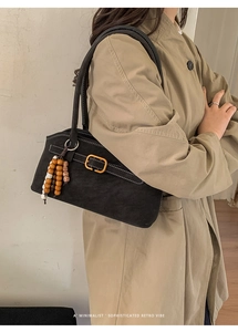 Detail der schwarzen Retro-Umhängetasche mit weißen Kontrastnähten und Holzperlenanhänger