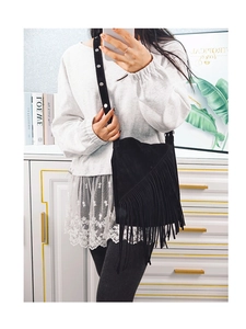 Close-up of black suede crossbody bag featuring dense tassels and studded wide shoulder strap