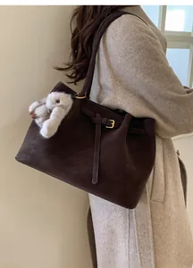 Détail d'un sac cabas en daim marron foncé avec boucle réglable et breloque lapin en peluche