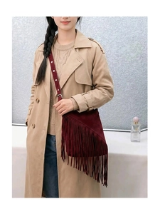 Detail of burgundy suede crossbody bag with long tassels on a model in a beige coat