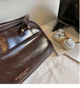 Detail of dark brown glossy leather bag with gold logo on a desk with laptop and books