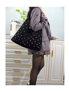 Detailed view of black suede tote bag with golden metal eyelets and thin shoulder strap
