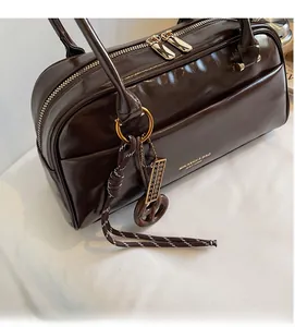 Macro detail of dark brown polished leather boston bag with gold zippers and abacus charm