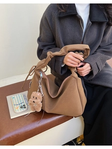 Brown suede hobo bag with pleated strap and teddy bear charm on leather bench