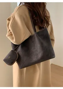Detalle de un bolso tote de ante gris oscuro con logotipo dorado y estilo bandolera