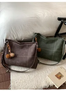 Detalle de bolsos tote de ante en café y verde con costuras de contraste y pompones