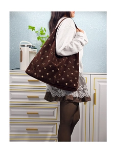 Detail of dark brown suede tote bag featuring polished gold metal eyelets and textured finish