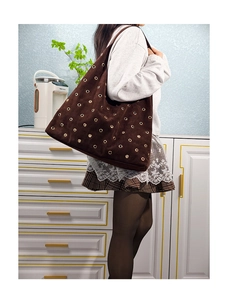 Detail of brown suede tote bag featuring decorative gold metal eyelets and soft texture