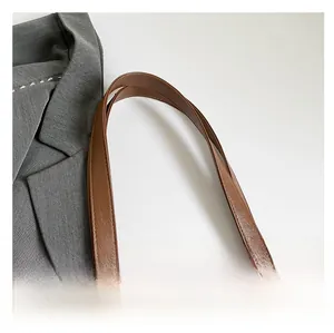 Detail of brown leather tote handle with reinforced stitching and metallic rivets