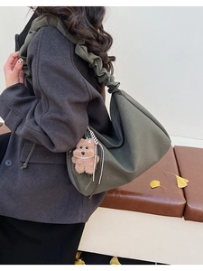 Olive green tote bag with pleated shoulder strap and plush puppy charm on a winter coat