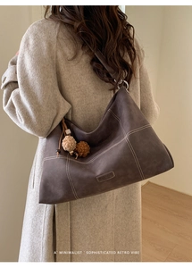 Deep gray leather tote bag featuring bold white contrast stitching and fluffy pom pom charms