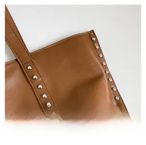 Close-up of brown leather bag with metallic silver studs and premium grainy texture