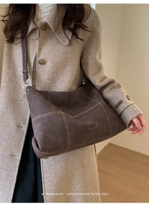 Detail of dark brown matte tote bag with contrast stitching on beige wool coat