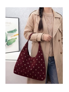 Detail of burgundy suede tote bag featuring metallic eyelets on khaki trench coat