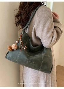 Detalle de bolso tote de ante verde con costuras de contraste y colgante de madera