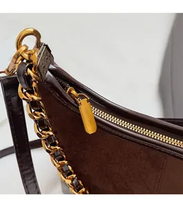 Close-up of brown patchwork leather bag with golden chain strap and smooth metal zipper