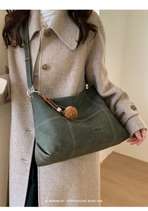 Detalle del bolso tote verde oscuro con costuras en contraste y pompon marrón