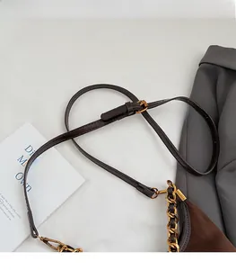 Detail of adjustable leather strap and gold chain on dark brown suede shoulder bag