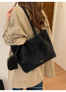 Bolso tote negro mate con monedero y logotipo dorado lucido sobre una gabardina beige