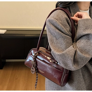 Détail d'un sac bowling en cuir verni bordeaux porté avec un blazer gris élégant