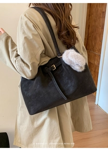 Detail of black large tote bag in matte suede leather with decorative belt buckle and charm
