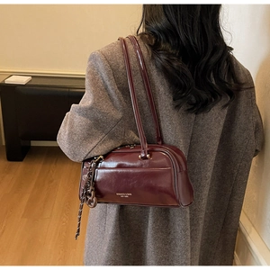Burgundy glossy leather Boston bag with shoulder strap worn over a grey wool coat