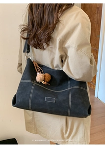 Primer plano del bolso tote de ante negro con costuras blancas en contraste y colgante suave