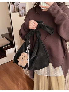Detail of black soft leather tote bag featuring a cute plush bear pendant and ruched handle