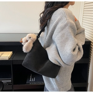 Close-up of black suede underarm bag with a cute plush puppy pendant and shoulder strap