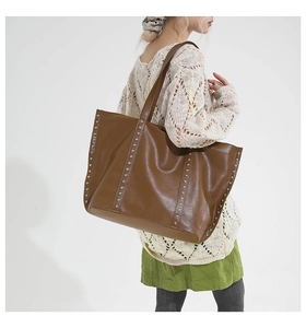 Brown tote bag with silver rivets and long straps shown on a model in beige knitwear