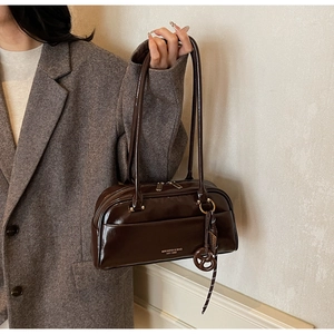 Détail d'un sac oreiller en cuir verni marron foncé avec fines anses et lettrage de marque