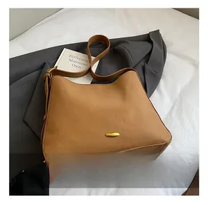 Detail view of brown matte leather tote bag with gold oval buckle on a cozy white bed