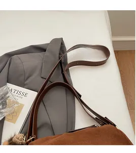 Detail einer braunen Wildlederhandtasche mit langem Lederriemen und Bommel-Anhänger
