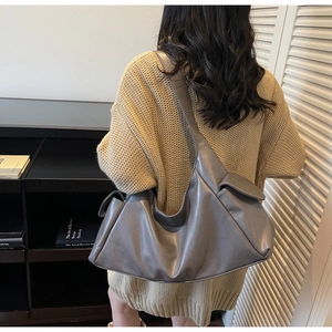 Minimalist grey leather hobo bag with side pockets shown as a crossbody shoulder bag