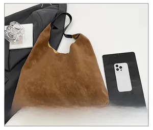 Brown frosted suede tote bag with black straps displayed on a desk with art books