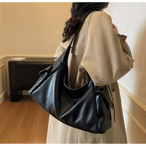 Gros plan d'un sac hobo noir mat avec poches latérales, porté par un mannequin en trench