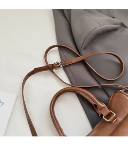 Detail of a brown leather handbag featuring silver metal buckles and an adjustable strap
