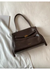 Macro detail of deep brown leather tote bag featuring gold metal buckle and logo