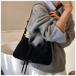 Detail of a black suede hobo bag featuring long fringe tassels and golden metal hardware