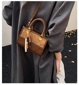 Detail of a brown patchwork crossbody bag with woven handles and a decorative tassel