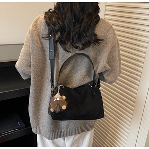 Close-up of black crossbody pillow bag with a playful fuzzy brown monster charm