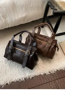 Détail de sacs Boston vintage en marron foncé et caramel sur un tapis blanc