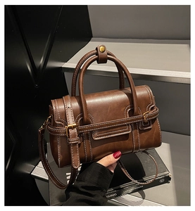 Detail view of a brown leather small square handbag with elegant white stitching and gold buckles.